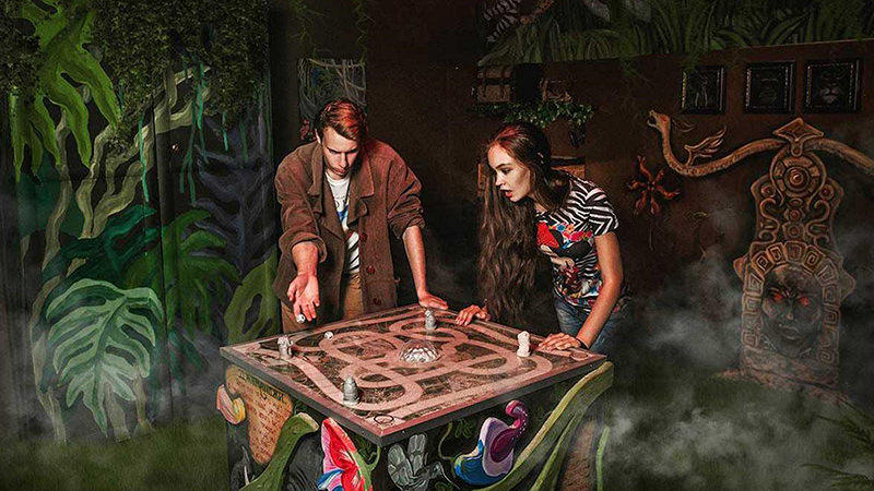 Two people play a tabletop game during a jungle escape quest.